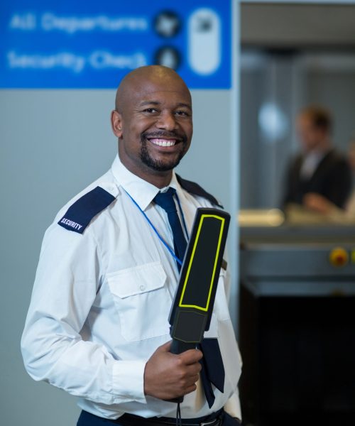 Smiling airport security officer holding metal detector in airport terminal
